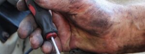 Imagen en primer plano de la mano de un mecánico, sucia, con un destornillador, arreglando un coche.